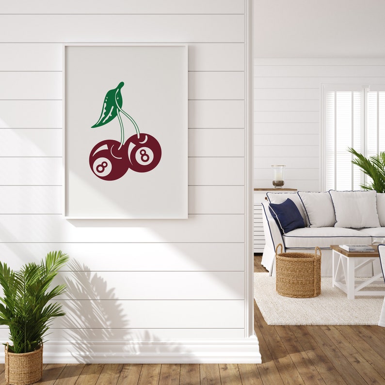 May include: A white framed print of a red cherry with a green stem and leaves. The cherry is a billiard ball with the number 8 on it.