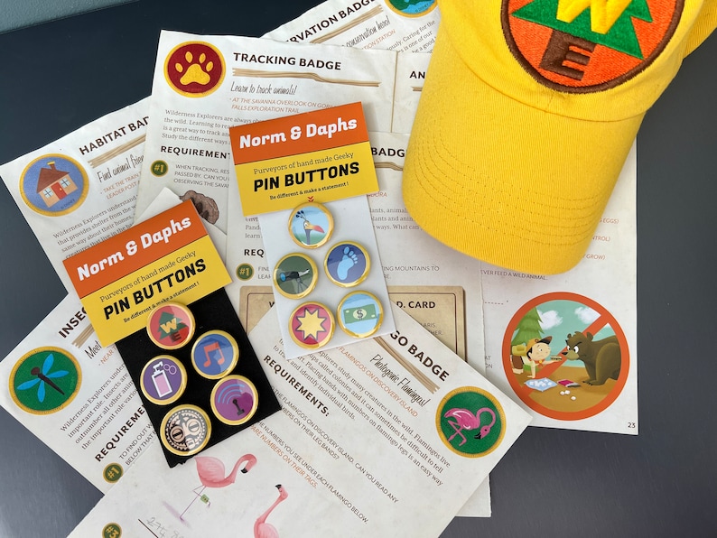 May include: A collection of pin buttons, a yellow cap, and printed cards. The pin buttons have gold rims and various designs. The cap has an embroidered patch. The cards feature text and illustrations, including a flamingo and a bear.