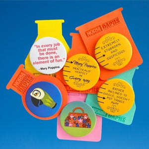 Könnte beinhalten: Eine Sammlung bunter Ansteckbuttons und Anhänger mit Zitaten und Illustrationen. Die Buttons zeigen Zitate aus Mary Poppins und andere skurrile Designs, darunter einen Papagei und eine florale Handtasche. Die Anhänger tragen den Text "NORM DAPHS".