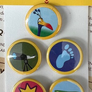 May include: Set of five round pin buttons with various designs. The buttons feature images of a bird, a telescope, a footprint, a starburst, and a dollar bill. The text "PIN BUTTONS" and "Be different & make a statement!" are visible.