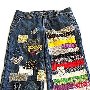 Könnte beinhalten: Blaue Jeans aus Denim mit bunten Patchwork-Stoffen, die auf der Vorder- und Rückseite der Beine aufgenäht sind. Das Patchwork umfasst verschiedene Farben, Muster und Texturen.
