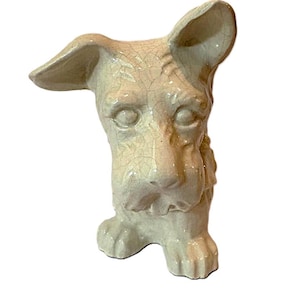 Könnte beinhalten: Cremefarbene Keramik-Hundefigur mit Craquelé-Glasur. Der Hund hat große Ohren und ein detailliertes Gesicht und steht auf seinen Vorderpfoten. Ein dekoratives Element für das Zuhause.