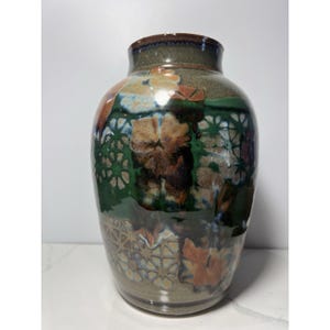 Könnte beinhalten: Eine Keramikvase mit breitem Körper und schmalem Hals. Die Vase weist eine Mischung aus Farben auf, darunter Braun, Grün, Orange und Blau. Das Design umfasst florale und geometrische Muster. Die Vase hat eine glänzende Oberfläche und ist wahrscheinlich handgefertigt.