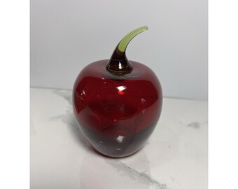 May include: A decorative glass apple sculpture. The apple is a deep red color with a dark base and a green stem. The glass is smooth and reflective, creating a glossy appearance. This art piece is a unique home decor item.