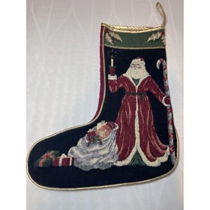 May include: A Christmas stocking with a black background and a gold trim. The stocking features an image of Santa Claus holding a candle, a sleeping child, and wrapped gifts. A candy cane is on the right side of the stocking.