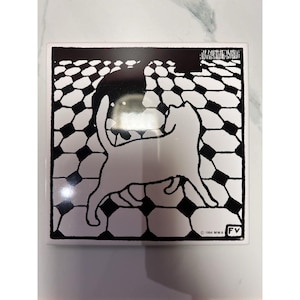 Puede incluir: Azulejo cerámico cuadrado con una ilustración de gato en blanco y negro. El gato es blanco, sobre un patrón geométrico en blanco y negro. El azulejo tiene el texto "©1994 MMA FV".