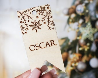 May include: A wooden Christmas gift tag with a snowflake design and the name "OSCAR" engraved on it.