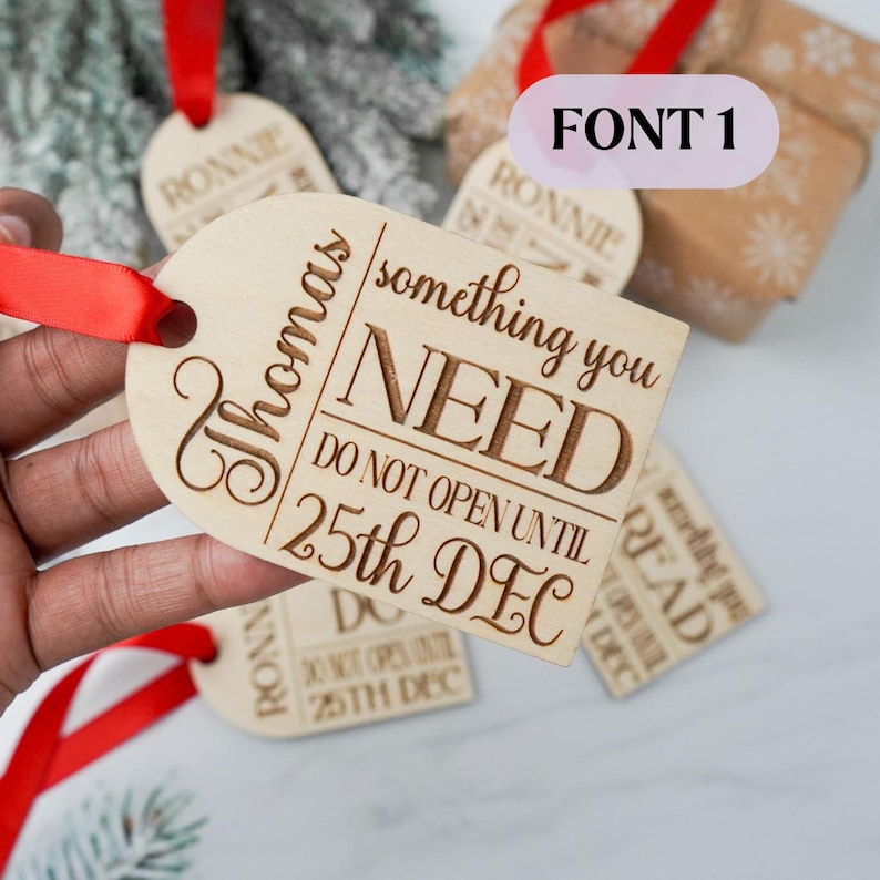 May include: Wooden gift tags with red ribbon. One tag reads "Thomas, something you NEED, DO NOT OPEN UNTIL 25th DEC." Other tags say "RONNIE" and "READ." The tags are light brown with engraved text.