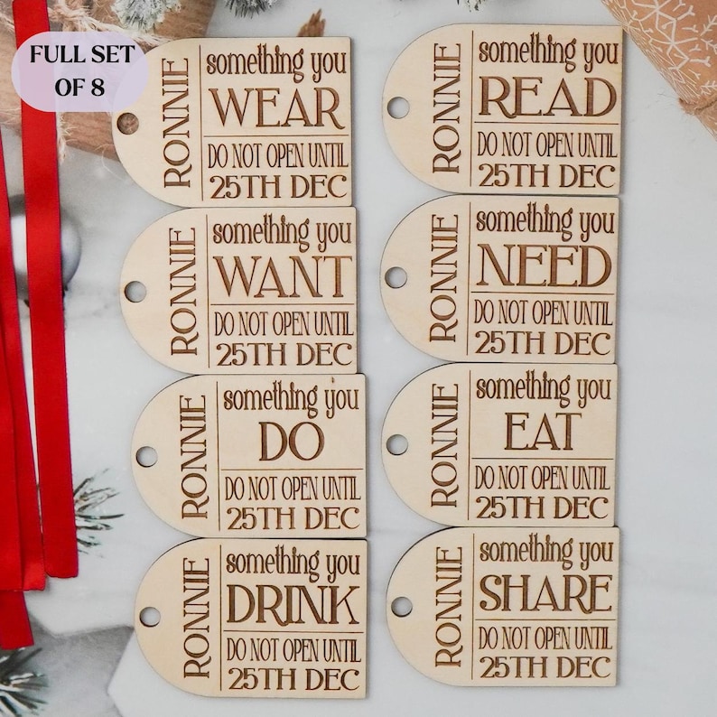 May include: A set of eight wooden gift tags with the name "Ronnie" and phrases like "Wear," "Read," and "Share" engraved on them. Each tag includes the text "Do not open until 25th Dec."