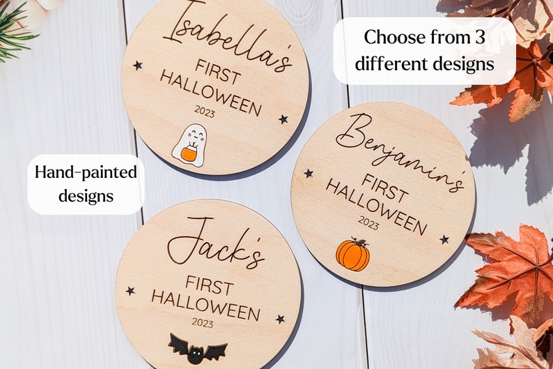 Puede incluir: Tres adornos redondos de madera con el texto "First Halloween 2023" y el nombre de un ni&ntilde;o. Los adornos presentan un fantasma, una calabaza y un murci&eacute;lago.