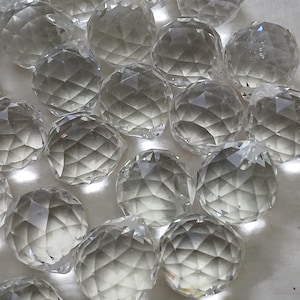 May include: A collection of clear, faceted crystal balls. Each sphere has a complex geometric pattern cut into its surface, reflecting light. The spheres are scattered on a white surface, creating a sparkling display.