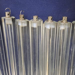 May include: Six clear, cylindrical glass tubes with silver metal caps and small hooks. The ribbed tubes are empty. The background is a dark blue fabric. Each tube is approximately 20 cm long.