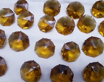 May include: A collection of 18 amber-colored glass crystal prisms with a faceted design. The prisms are arranged in a random pattern on a white surface.
