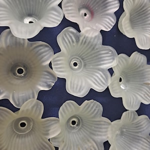 May include: A collection of frosted glass flower-shaped components. Each flower has five petals with delicate veining and a central hole. The flowers are arranged on a dark blue textured surface, creating a pattern.