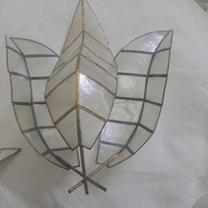 May include: A decorative, three-leaf shaped object with a metallic gold frame and iridescent, shell-like panels. The leaves are arranged in a fan shape, with a cross-shaped base. The object is likely a decorative piece for a home.