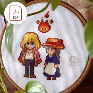 Pode incluir: Bordado em ponto cruz em um bastidor de madeira com personagens de um filme de animação popular. O design inclui duas figuras e uma criatura de fogo, tudo em estilo pixelado. O ícone PDF é visível.