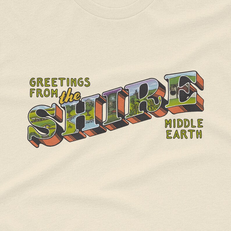 May include: A cream colored t-shirt with a vintage postcard design featuring the words "Greetings from the Shire" in a colorful, stylized font. The postcard also includes the words "Middle Earth" in a smaller font.