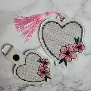 May include: Two white heart-shaped keychains with pink floral embroidery and a pink tassel.