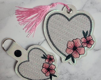 Puede incluir: Dos llaveros blancos en forma de corazón con bordado floral rosa y un borla rosa.
