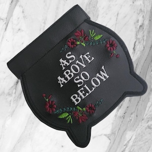 May include: A black cauldron-shaped patch featuring white embroidered text that reads AS ABOVE SO BELOW. The design is accented with embroidered floral motifs in shades of deep red and bright green, arranged in a semi-circular pattern around the text.