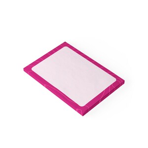Op de afbeelding: Een rechthoekig notitieblok met een witte binnenkant en een felroze rand. De roze rand heeft een subtiel, abstract ontwerp. Het notitieblok staat schuin tegen een witte achtergrond en toont zijn strakke lijnen en moderne esthetiek.