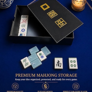 May include: A black mahjong storage box with gold Chinese characters on the lid, containing white and light blue tiles. The set includes various tiles with symbols and numbers, displayed alongside text that reads PREMIUM MAHJONG STORAGE.