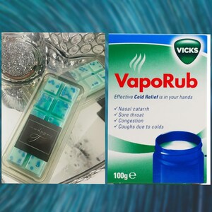 May include: A teal blue wax melt with a Vicks VapoRub label in the background. The wax melt is in a clear plastic container and has a white label with the text "microbreathing".