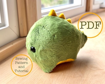 May include: A green and yellow plush dinosaur toy with a cute face. The toy is lying on a wooden surface. The text "Sewing Pattern and Tutorial" is written in a circle around the toy. The text "PDF" is written in a circle in the top right corner of the image.