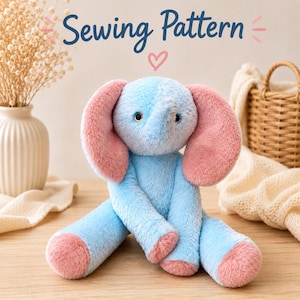 Op de afbeelding: Een pluche olifant met lichtblauwe vacht en roze accenten op de oren en voeten. De olifant heeft donkere ogen en zit rechtop. Boven het speelgoed staat de tekst Sewing Pattern in donkerblauw schrift met een klein roze hartje eronder.