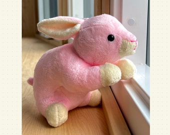 May include: A pink plush bunny toy with yellow ears and a black eye. The bunny is 19cm long and 11.5cm tall.