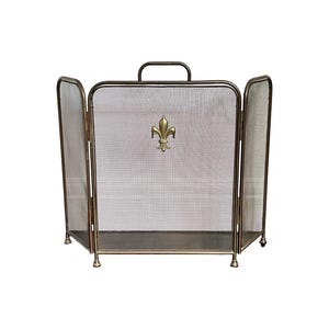 May include: A three-panel fireplace screen made of bronze-toned metal mesh. The central panel features a prominent gold-colored fleur-de-lis emblem. The screen includes a top handle and stands on four small, rounded feet, providing a structured barrier.
