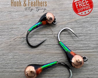 May include: Three fishing flies featuring a metallic copper bead head, a black body section, and a vibrant iridescent green and orange segmented tail. Each fly is constructed on a curved dark metal hook, with one fly showing thin, wispy tail fibers.