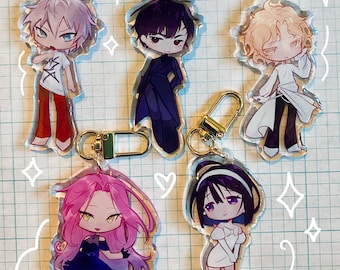 Op de afbeelding: Vijf kleurrijke anime-personage sleutelhangers met gouden metalen ringen. De personages zijn getekend in chibi-stijl en omvatten een jongen met wit haar en een rode broek, een jongen met zwart haar en een zwart pak, een jongen met blond haar en een wit shirt, een meisje met roze haar en een paarse jurk en een meisje met zwart haar en een witte jurk.