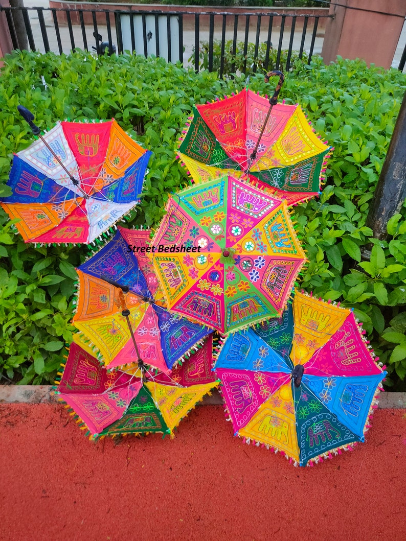 Puede incluir: Cinco paraguas coloridos con dise&ntilde;os bordados, incluyendo elefantes, flores y patrones geom&eacute;tricos. Los paraguas est&aacute;n hechos de tela y tienen mangos de madera.