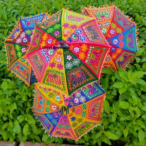 Puede incluir: Un conjunto de cuatro paraguas coloridos con bordados intrincados y adornos de espejo. Los paraguas est&aacute;n decorados con motivos florales y elefantes. Los paraguas est&aacute;n apilados, con el paraguas superior parcialmente abierto.