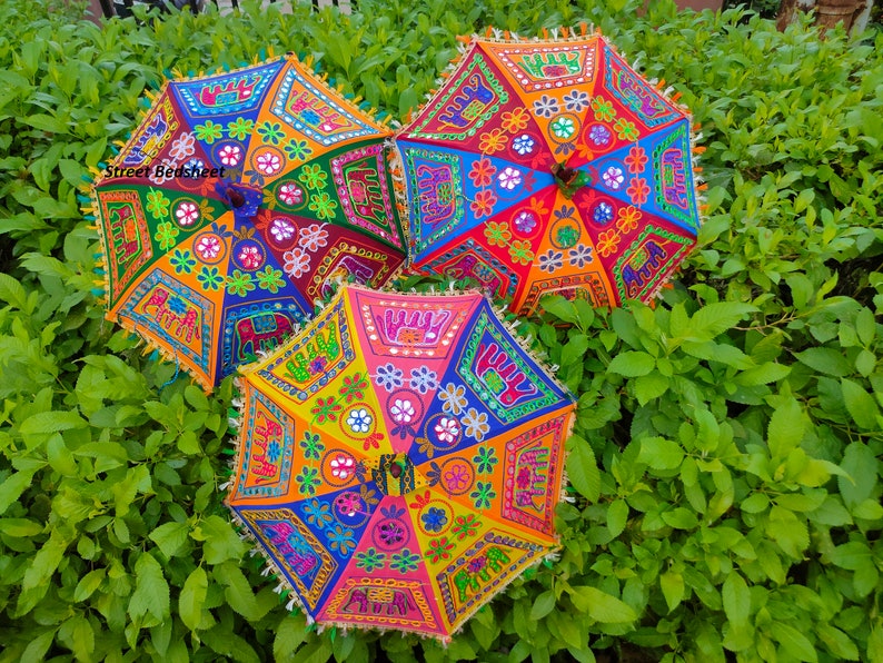 Puede incluir: Tres paraguas coloridos con bordados intrincados y trabajo de espejo. Los paraguas est&aacute;n decorados con patrones florales, formas geom&eacute;tricas y elefantes. Los paraguas son una mezcla vibrante de rojo, naranja, amarillo, verde, azul y morado.