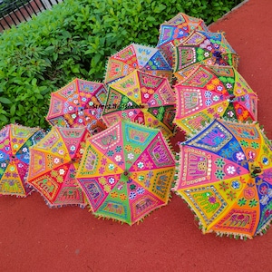 Puede incluir: Una colecci&oacute;n de paraguas bordados coloridos con dise&ntilde;os intrincados, incluyendo elefantes y flores. Los paraguas est&aacute;n decorados con lentejuelas y espejos, creando un aspecto festivo y vibrante.
