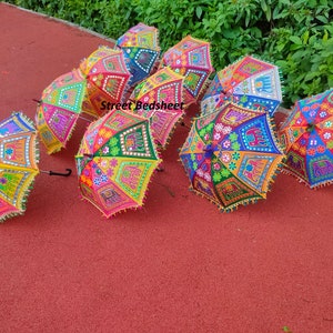 Puede incluir: Un grupo de paraguas coloridos, bordados con detalles de espejo. Los paraguas est&aacute;n dispuestos sobre una superficie roja. Los paraguas est&aacute;n decorados con motivos florales, elefantes y otros motivos.