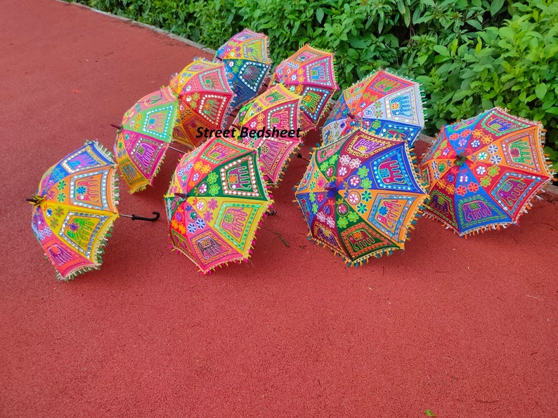 Puede incluir: Un grupo de paraguas coloridos, bordados con detalles de espejo. Los paraguas est&aacute;n dispuestos sobre una superficie roja. Los paraguas est&aacute;n decorados con motivos florales, elefantes y otros motivos.