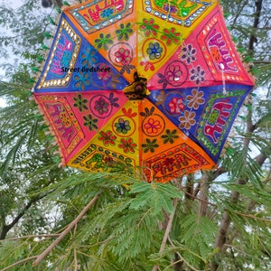 Puede incluir: Un paraguas colorido de varias capas con dise&ntilde;os bordados de flores y elefantes. El paraguas est&aacute; hecho de tela y tiene una combinaci&oacute;n de colores brillantes amarillo, naranja, rosa, azul y verde. El paraguas est&aacute; decorado con lentejuelas y espejos.