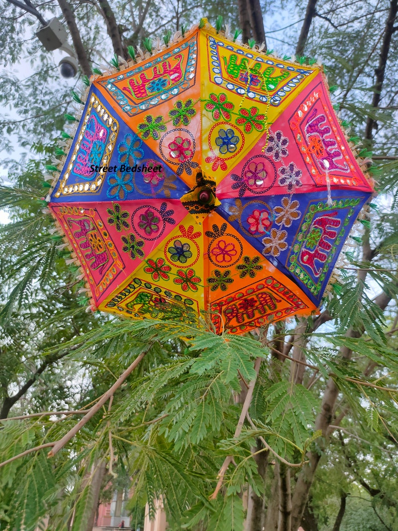 Puede incluir: Un paraguas colorido de varias capas con dise&ntilde;os bordados de flores y elefantes. El paraguas est&aacute; hecho de tela y tiene una combinaci&oacute;n de colores brillantes amarillo, naranja, rosa, azul y verde. El paraguas est&aacute; decorado con lentejuelas y espejos.
