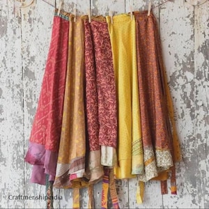 May include: A collection of five wrap skirts hanging from a line, featuring various patterns and colors including red, gold, yellow, and brown. Each skirt displays distinct floral and geometric prints with layered fabric panels and hem details.