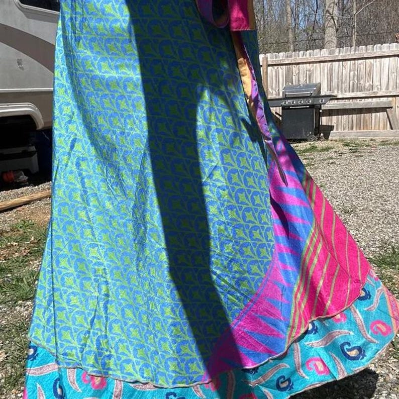 May include: A long wrap skirt featuring a vibrant blue and lime green geometric pattern on the main panel, contrasted by a bright pink and blue striped section and a bottom border decorated with a colorful paisley print in shades of blue and pink.
