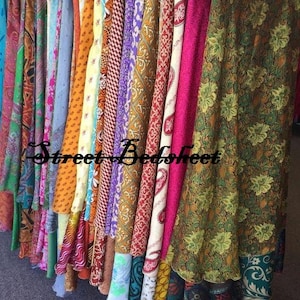 May include: A collection of long skirts hanging on a rack, featuring a variety of colorful fabrics with diverse patterns including floral, paisley, and geometric designs. The text Street Bedsheet is overlaid across the center of the hanging garments.