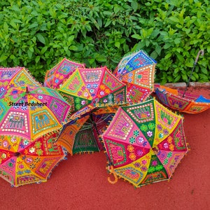 Puede incluir: Un grupo de paraguas coloridos y estampados con detalles bordados y acentos de espejo. Los paraguas est&aacute;n dispuestos en c&iacute;rculo sobre una superficie roja.