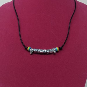 May include: A black cord necklace with a rainbow bead and silver charm beads spelling out "JERSEY".