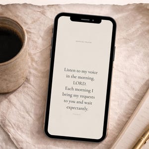 Puede incluir: Un teléfono inteligente muestra el texto "MORNING PRAYER" y una oración. También se ven una taza de café, un bolígrafo y un bloc de notas. Las palabras "Inspire your mornings" están en la parte inferior.