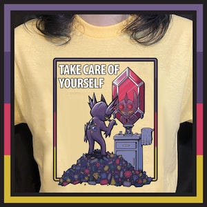May include: Yellow t-shirt with a graphic featuring a purple creature looking in a red crystal mirror. The text "TAKE CARE OF YOURSELF" is above the image. The creature stands on a pile of colorful gems.