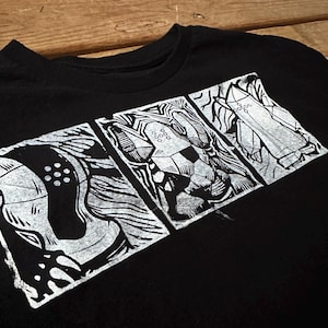 May include: Black t-shirt featuring a white graphic design in three panels. The design appears to be an abstract illustration with intricate linework. The shirt is made of a soft material and has a crew neck.