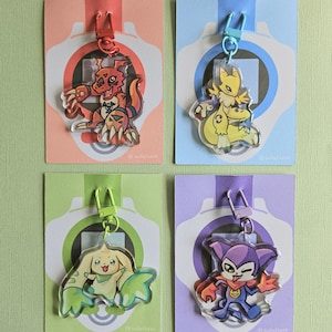 Peut inclure: Quatre porte-clés en acrylique représentant des personnages de dessins animés, chacun avec une palette de couleurs différente. Les porte-clés sont attachés à des cartes colorées avec un design assorti. Les personnages sont en rouge, jaune, vert et violet.